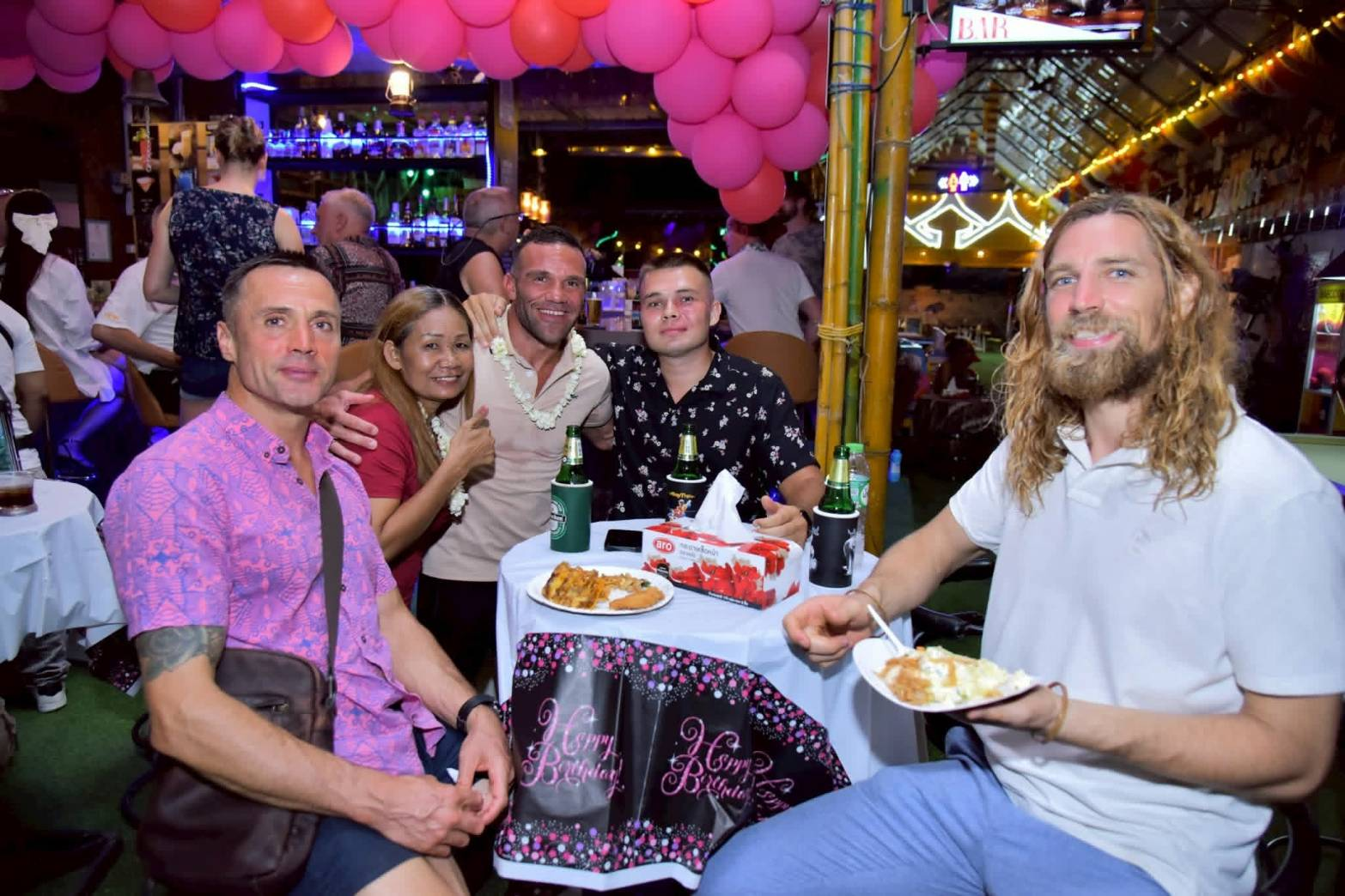Friends celebrating at a table with beers and a Happy Birthday tablecloth