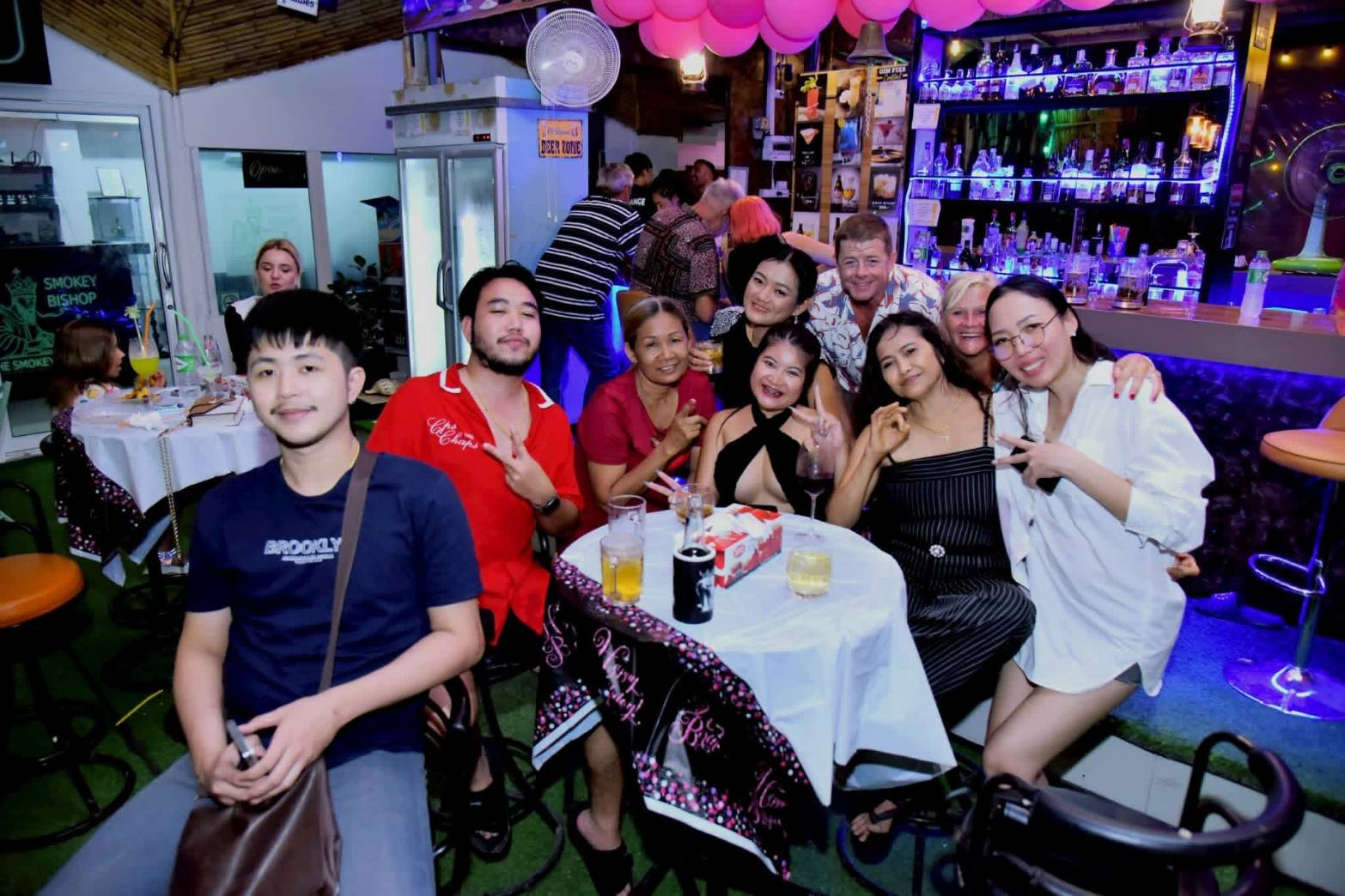 A lively group of customers raising peace signs at a table in front of the stocked bar