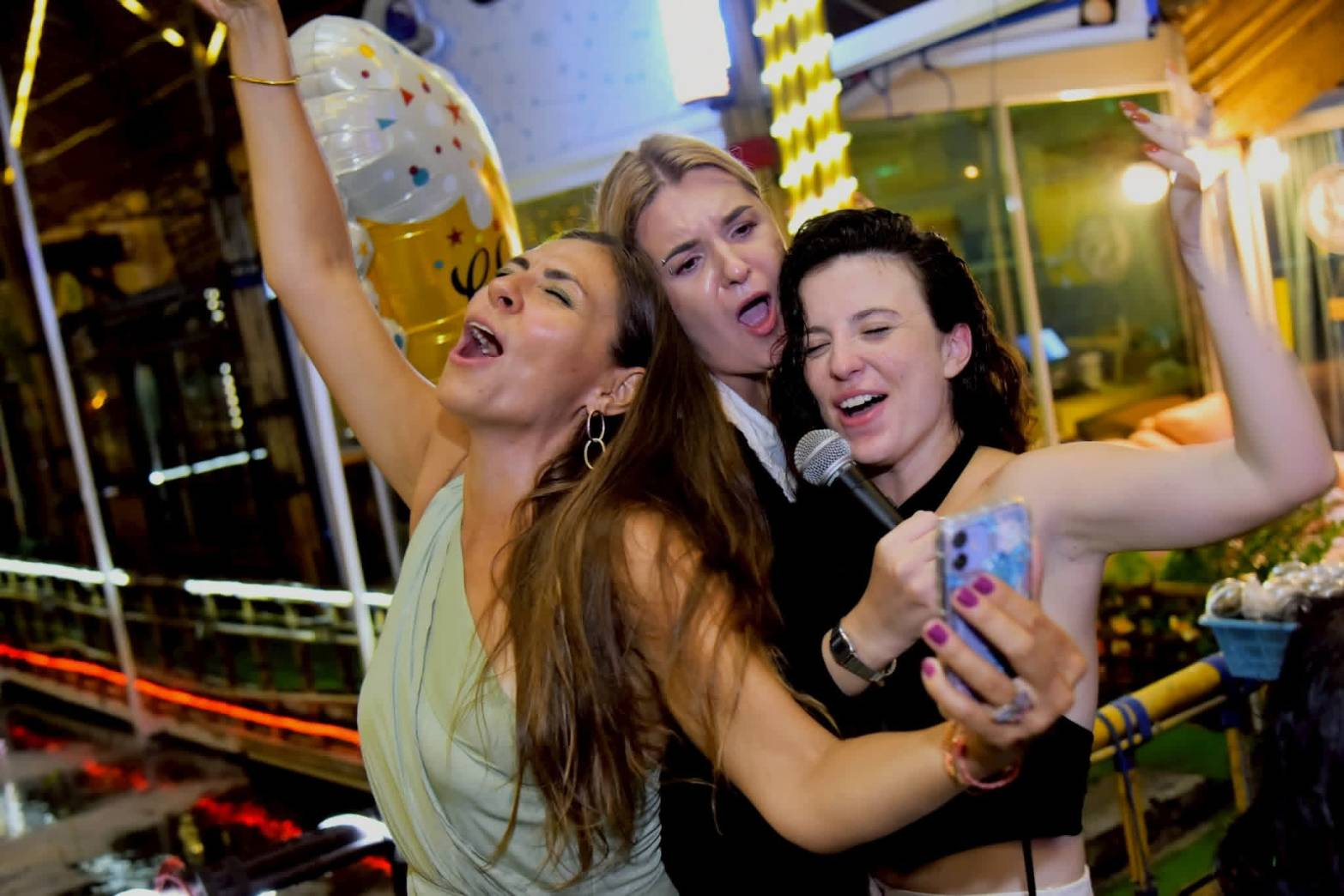 Three friends singing together into a microphone during a fun night out